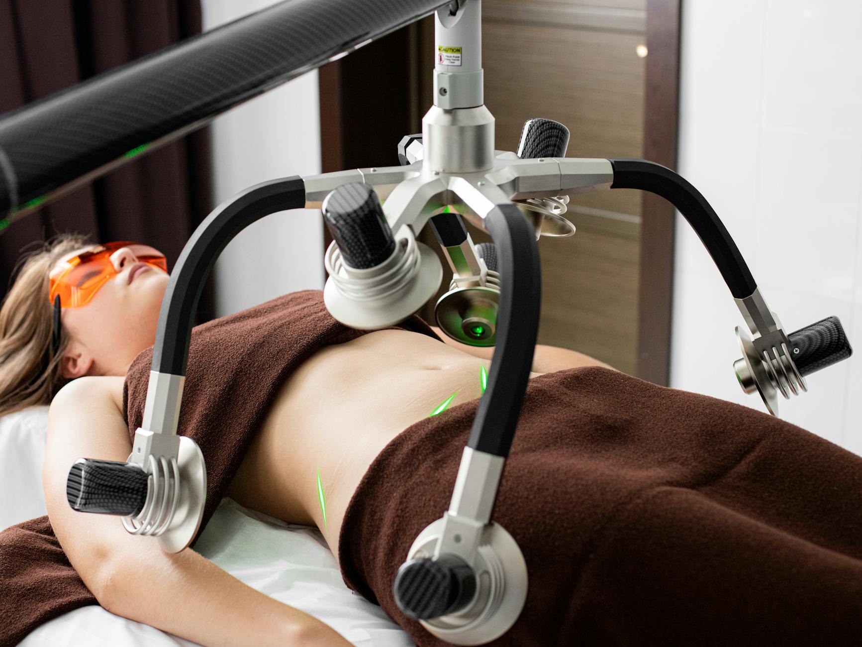 PowerSlim w domu i w salonie: kompletny przewodnik po urządzeniach na ciało Kobieta podczas zabiegu odchudzającego PowerSlim z laserami na brzuchu